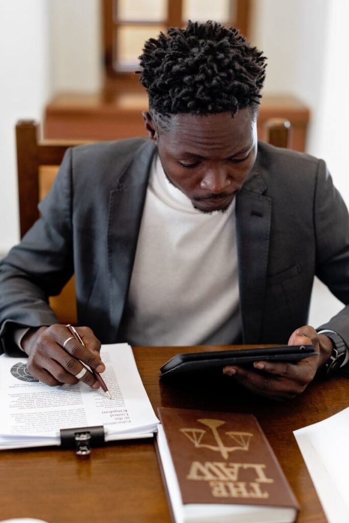 Businessman in black suit working with documents and tablet at an office desk.
